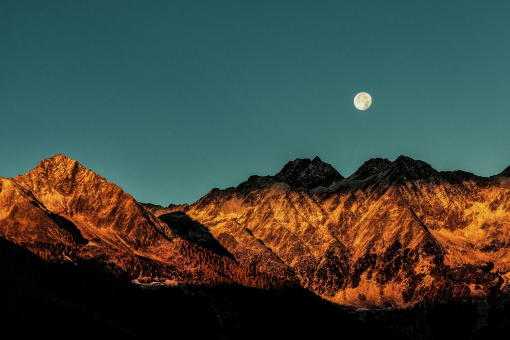 Breathtaking view of mountains with a full moon at twilight, capturing nature's beauty.